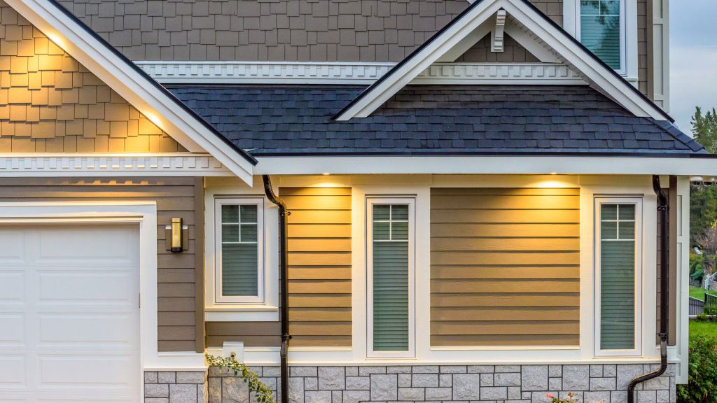 The image showcases the exterior of a modern house with beige horizontal siding, a white-framed window by ABC Seamless, and a blue shingle roof. Warm lights illuminate the entrance area, creating a welcoming appearance.