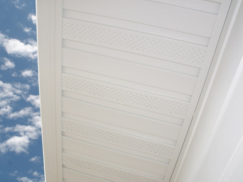 View of a white vinyl soffit with vents, attached under a building's roofline, set against a blue sky with scattered clouds.